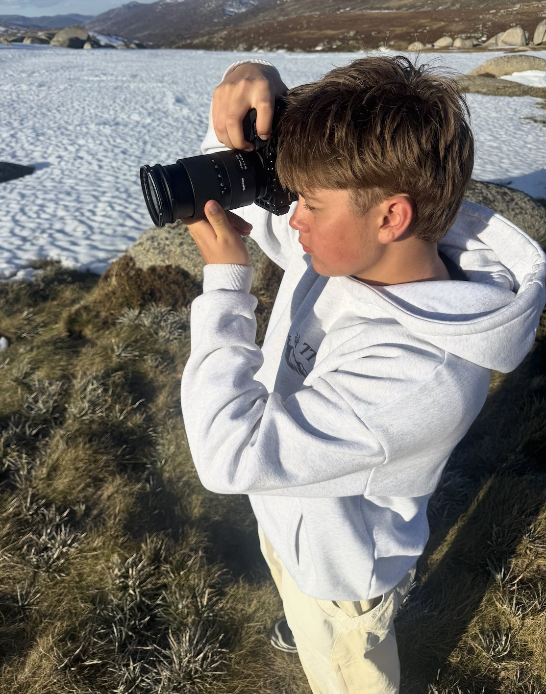 Finn lining up a shot with his camera in the snow, mountains behind him